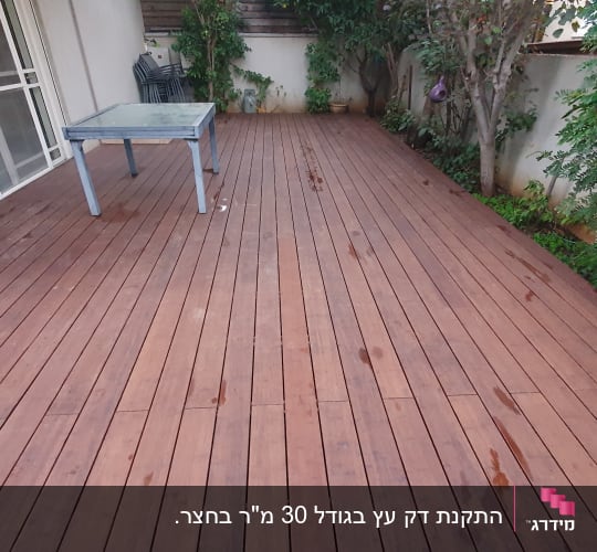 דק עץ עם שולחן זכוכית ועצים מסביב
